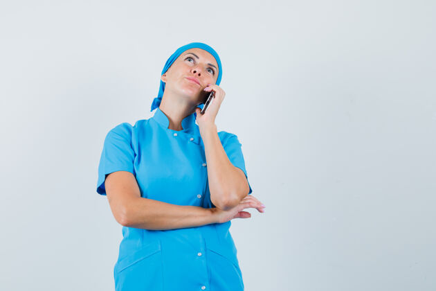 电话穿着蓝色制服的女医生在讲手机 看上去很体贴 前视图思想病人成年人