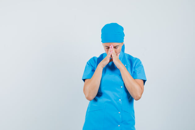 治疗身穿蓝色制服的女医生双手合十祈祷 看上去充满希望 正前方祈祷诊所疾病