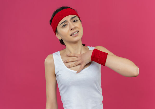 手掌穿着运动服的年轻健身女士戴着头巾站在粉红色的墙上 脸上挂着一张愁容满面的手掌健身脸姿势