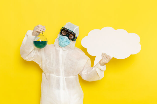 防护罩正面图：身着特殊套装的男科学工作者 在黄色的桌子上拿着装有绿色溶液和白色大标牌的烧瓶烧瓶服装化学