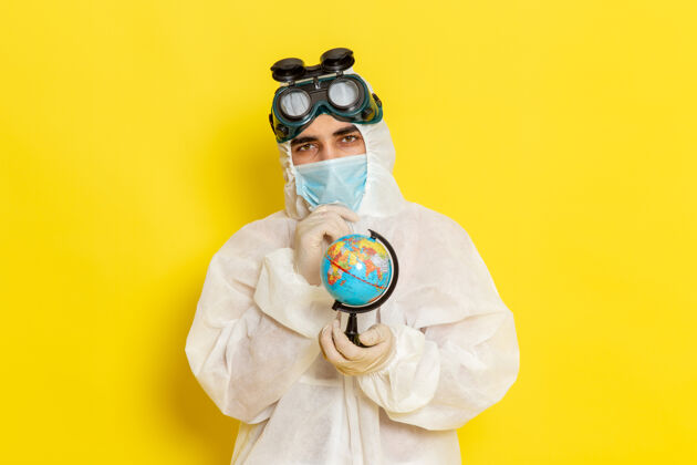 桌子正面图：一位身着特殊套装的男科学工作者 在黄色的桌子上拿着小地球仪地球仪前面外套