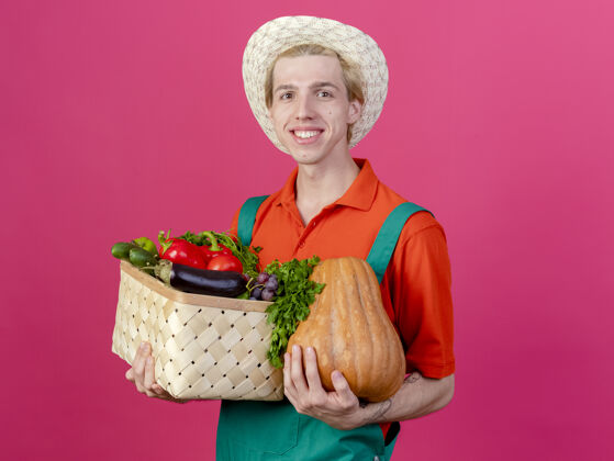 年轻人年轻的园丁穿着连体衣戴着帽子拿着装满蔬菜的箱子连身衣快乐花园