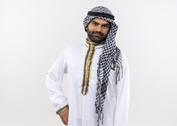 脸身着传统服装的阿拉伯男子站在白墙上 脸上带着自信的微笑看传统阿拉伯语