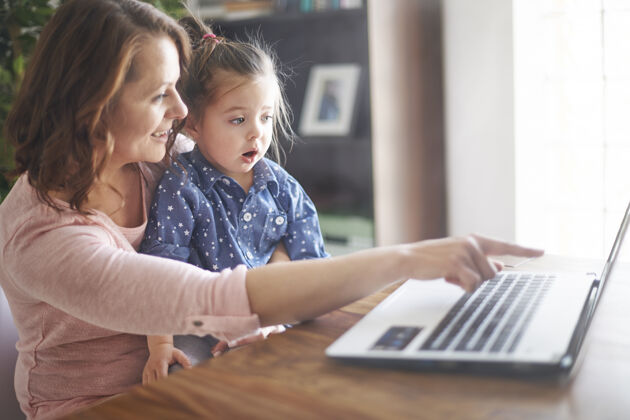 拥抱母女俩在笔记本电脑上看视频玩父母桌子