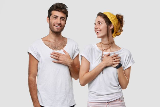 设计善良的白种男人和漂亮的女人手放在胸前 表示感谢 有友好的关系 靠着白墙站着高兴朋友积极