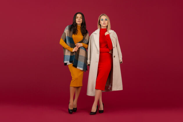 时尚两位穿着秋冬时装礼服和外套的时尚女性在红墙上孤零零地摆着姿势姿势夹克购物