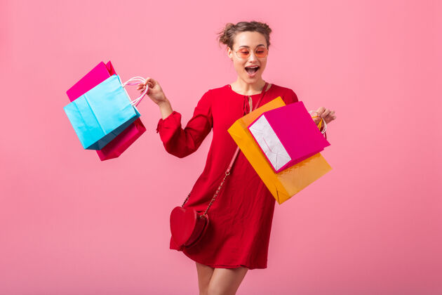 长度迷人的快乐微笑的时尚女性购物狂穿着红色的新潮连衣裙拿着五颜六色的购物袋在粉色的墙上孤立着 销售兴奋 时尚潮流夏天女性可爱