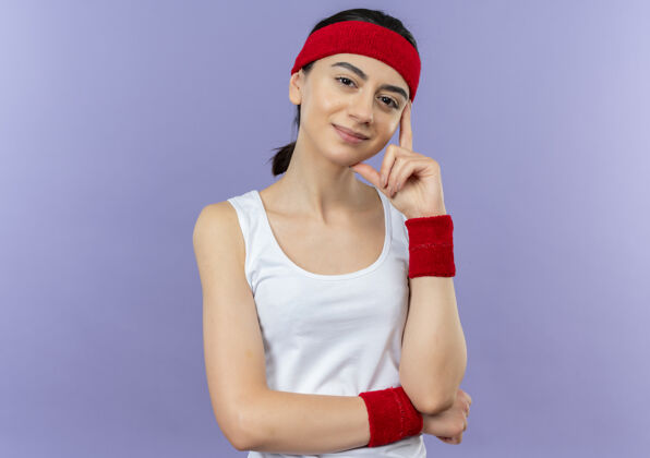 健身身穿运动服 头戴头巾 脸上带着自信微笑的年轻健身女士站在紫色的墙上女人运动人