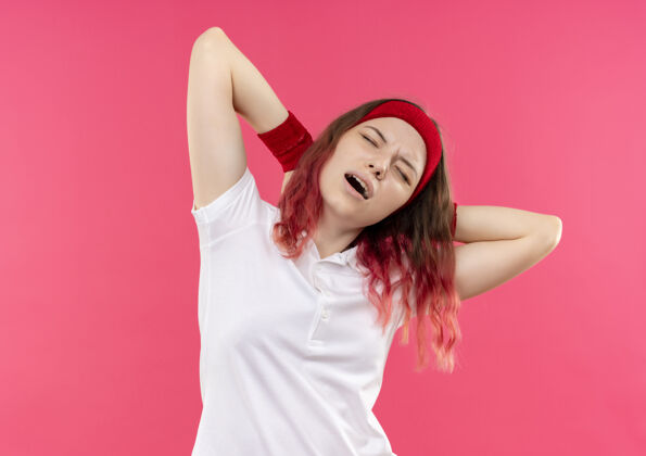 靠边戴着头巾的年轻运动型女人站在粉红色的墙上 困惑地看着一边 摸着脖子 疼得要命脖子女人看