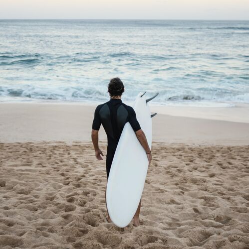 夏季穿着冲浪服的男人从后面走在沙滩上冒险冲浪生活方式