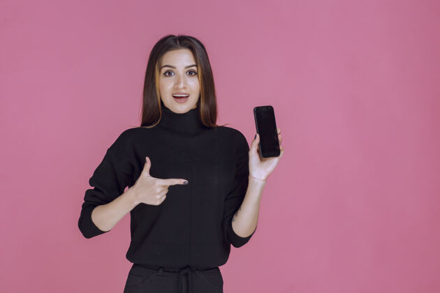 年轻穿着黑色毛衣的女人拿着一部智能手机指着它客户成人年轻人