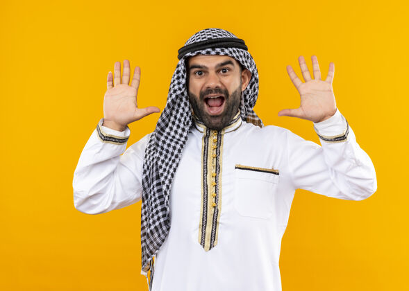 阿拉伯语身着传统服装的阿拉伯商人举手投降 站在橙色的墙壁上显得很惊讶惊喜商人投降