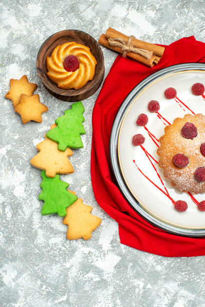 顶部顶视图白色椭圆形盘子上的浆果蛋糕红色披肩圣诞树饼干灰色表面午餐椭圆形蔬菜