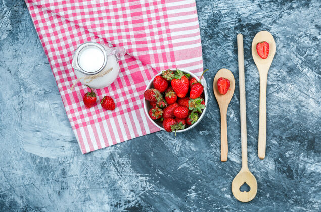 碗俯视图：一碗草莓和一壶牛奶放在红色方格毛巾上 深蓝色大理石表面放着木勺水平食物草莓有机