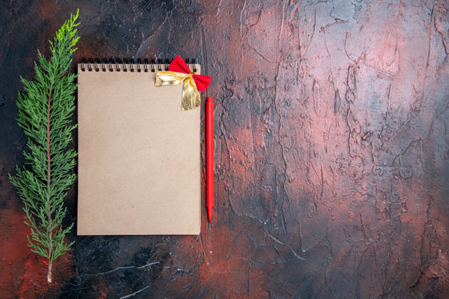 树枝顶视图红色钢笔一个小蝴蝶结的记事本一个松树枝在暗红色的表面上有复印的地方小地方年龄