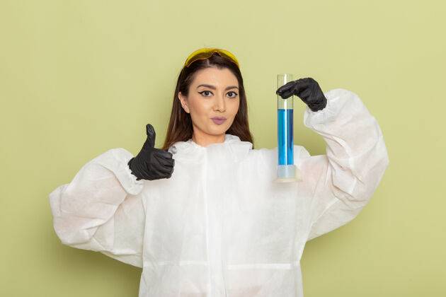 实验室外套前视图穿着特殊防护服的女化学家拿着装有蓝色溶液的烧瓶 在绿色表面摆姿势实验室溶液化学