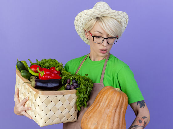 板条箱一位年轻的园丁 围着围裙 戴着帽子 手里拿着装满蔬菜的箱子短裤严肃的年轻的