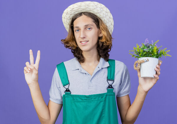 锅年轻的园丁 穿着连体衣 戴着帽子 微笑着捧着盆栽植物表演花园连身衣