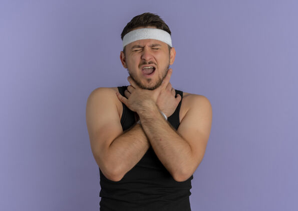 疼痛一个年轻的健身男子 戴着头巾 站在紫色的墙上疼得要命年轻教练健身