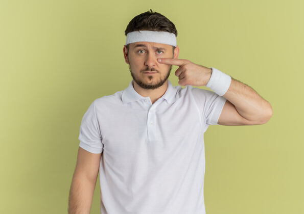 运动装一个身穿白衬衫 戴着头巾 手指着眼睛站在橄榄墙上的年轻健身男子男性橄榄健康