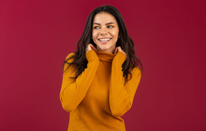 模特美丽的微笑 时尚的深色皮肤 穿着黄色秋冬时装毛衣的西班牙女人的画像 在红墙上摆出孤立的姿势年轻衣服秋天