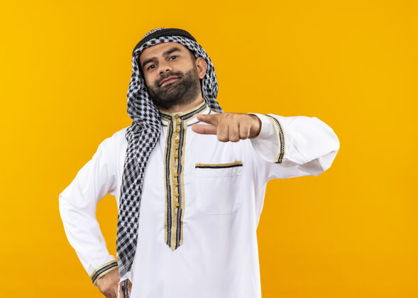 自信身着传统服饰的阿拉伯商人手指微笑自信地站在橙色的墙上阿拉伯语站立传统