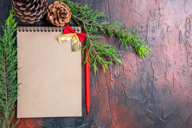 圣诞节顶视图红笔一本笔记本 用小蝴蝶结松树枝松果在暗红色的表面自由活动视图蝴蝶结背景
