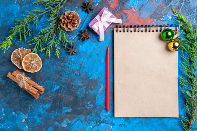 松树俯瞰笔记本上的圣诞球松树树枝桂皮棒八角干柠檬片蓝色表面顶部视图茴香