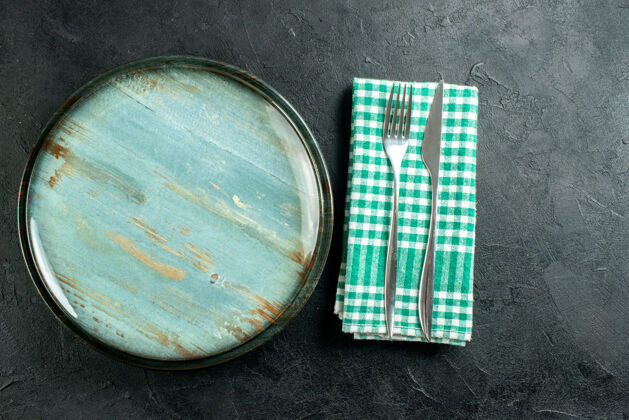 刀顶视图圆形餐盘餐刀和餐叉上绿色和白色方格餐巾上黑色桌子的自由空间观点盘子餐巾