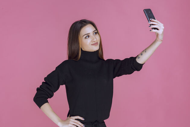年轻人一个穿着黑色毛衣的女人拿着一部智能手机自拍女性媒体姿势