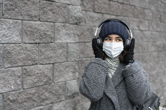 新常态戴着医用口罩的女人在城里用耳机听音乐病毒妇女流行病