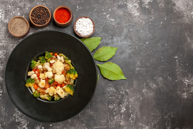 烤箱顶视图西兰花和花椰菜沙拉在黑碗里不同的香料在碗里叶子在黑暗的表面与副本sapce碗顶部花椰菜和花椰菜