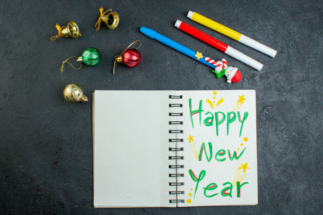 铅笔盒黑色背景上带新年快乐书写装饰配件的螺旋笔记本俯视图圣诞节观点钢笔