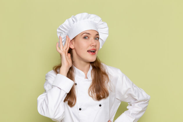 头饰身穿白色厨师服的女厨师在绿墙上努力倾听声音的正面视图淋浴帽帽子护士