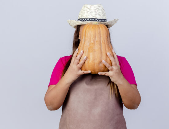 南瓜围裙戴帽子的中年园丁妇女站在白色背景下 手里拿着南瓜遮住脸年龄帽子围裙