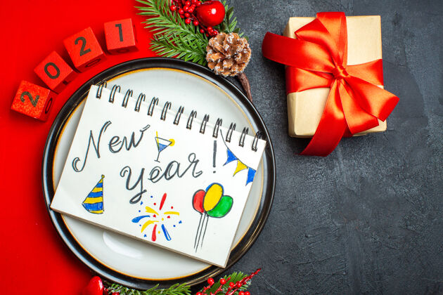 餐巾新年背景俯视图 餐盘上印有新年图画的笔记本装饰配件 红色餐巾上有杉木树枝和数字 黑色桌子上有礼物画视图树枝