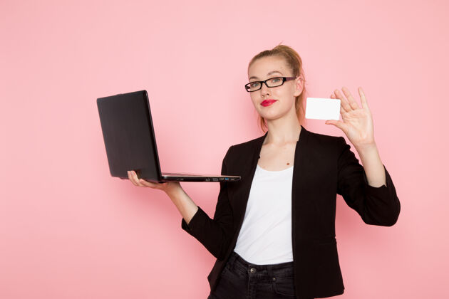 女身穿黑色夹克的女上班族正对着粉色墙上拿着名片 用笔记本电脑前面严格电脑