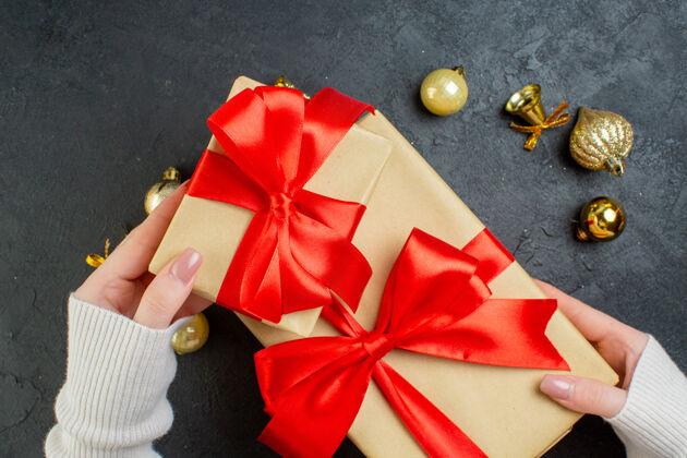车轮手持一个带有红丝带的礼品盒和深色背景上的装饰配件的俯视图圣诞节礼品盒顶部
