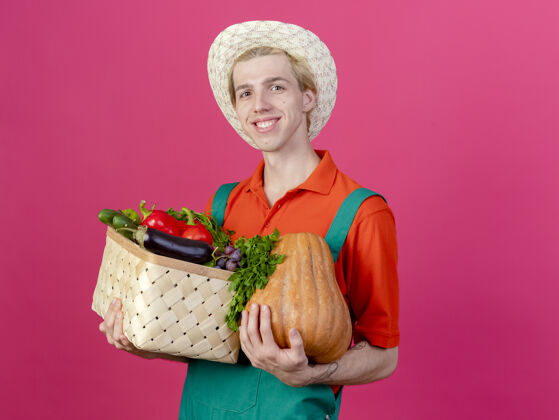 年轻人年轻的园丁穿着连体衣戴着帽子拿着装满蔬菜的箱子穿着脸连身衣