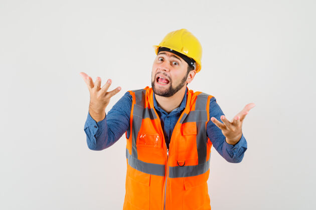 工具年轻的建筑工人穿着衬衫 背心 戴着头盔 做着提问的姿势 神情茫然 俯视前方工程师设备肖像