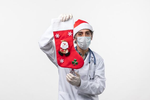 喜剧演员正面图男性医生拿着节日袜子在白色办公桌上-圣诞病毒健康制服病毒男医生