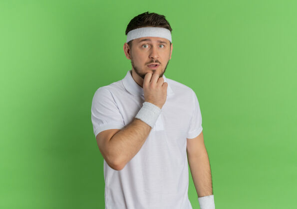 人身穿白衬衫 头戴头巾的年轻健身男子站在绿色的墙上 茫然地看着前方男人小伙子运动