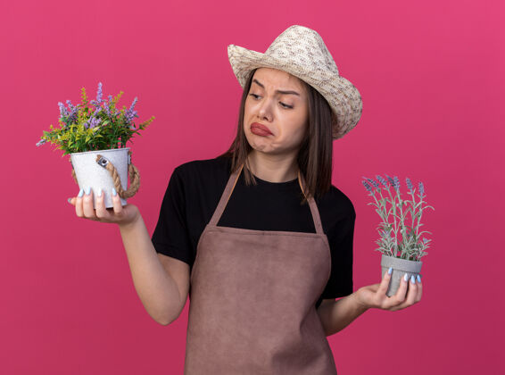 印象漂亮的白人女园丁戴着园艺帽 手拿花盆 看着粉色墙壁上孤立的复制空间帽子看花园