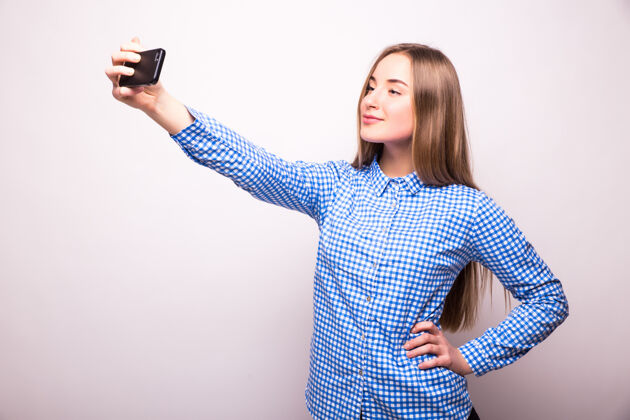 拍摄快乐调情的年轻女孩在智能手机前拍照 越过白墙电话移动自我