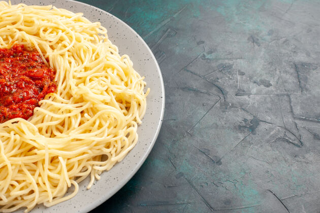 晚餐正面近距离观看煮熟的意大利面食 深蓝色表面有肉末和番茄酱调味品前面封闭