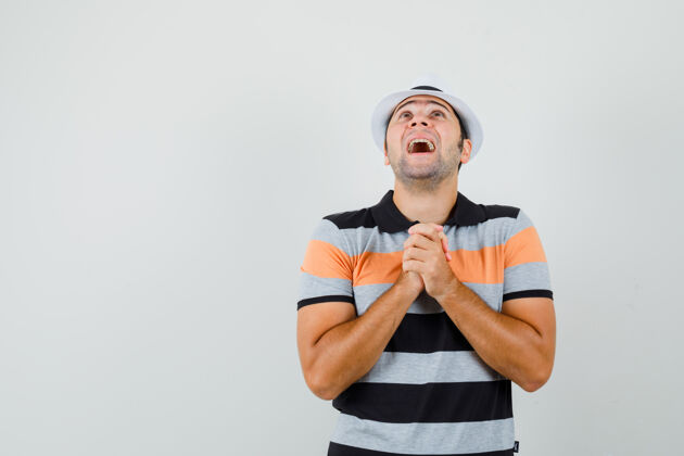 祈祷一个穿着条纹t恤 戴着帽子的年轻人展示着祈祷的姿态 期待着文本的空间商人成功衬衫