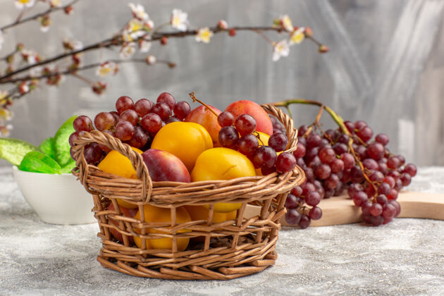 葡萄正面是新鲜甜美的杏子 篮子里有李子 白色桌子上有葡萄前面甜食李子