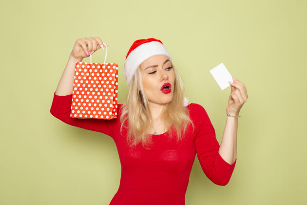 颜色正面风景美丽的女性拿着小包装礼物和银行卡在绿色的墙上情感节日圣诞节雪彩新年小银行雪