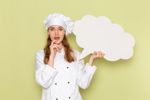 前面身穿白色厨师服的女厨师手持绿色墙上的白色标志的正面视图头饰淋浴肖像