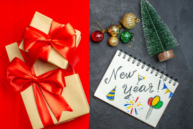 顶部俯视美丽的礼物与蝴蝶结形彩带笔记本与新年图纸旁边的杉树树枝装饰配件圣诞树上的红色背景树枝杉木书签